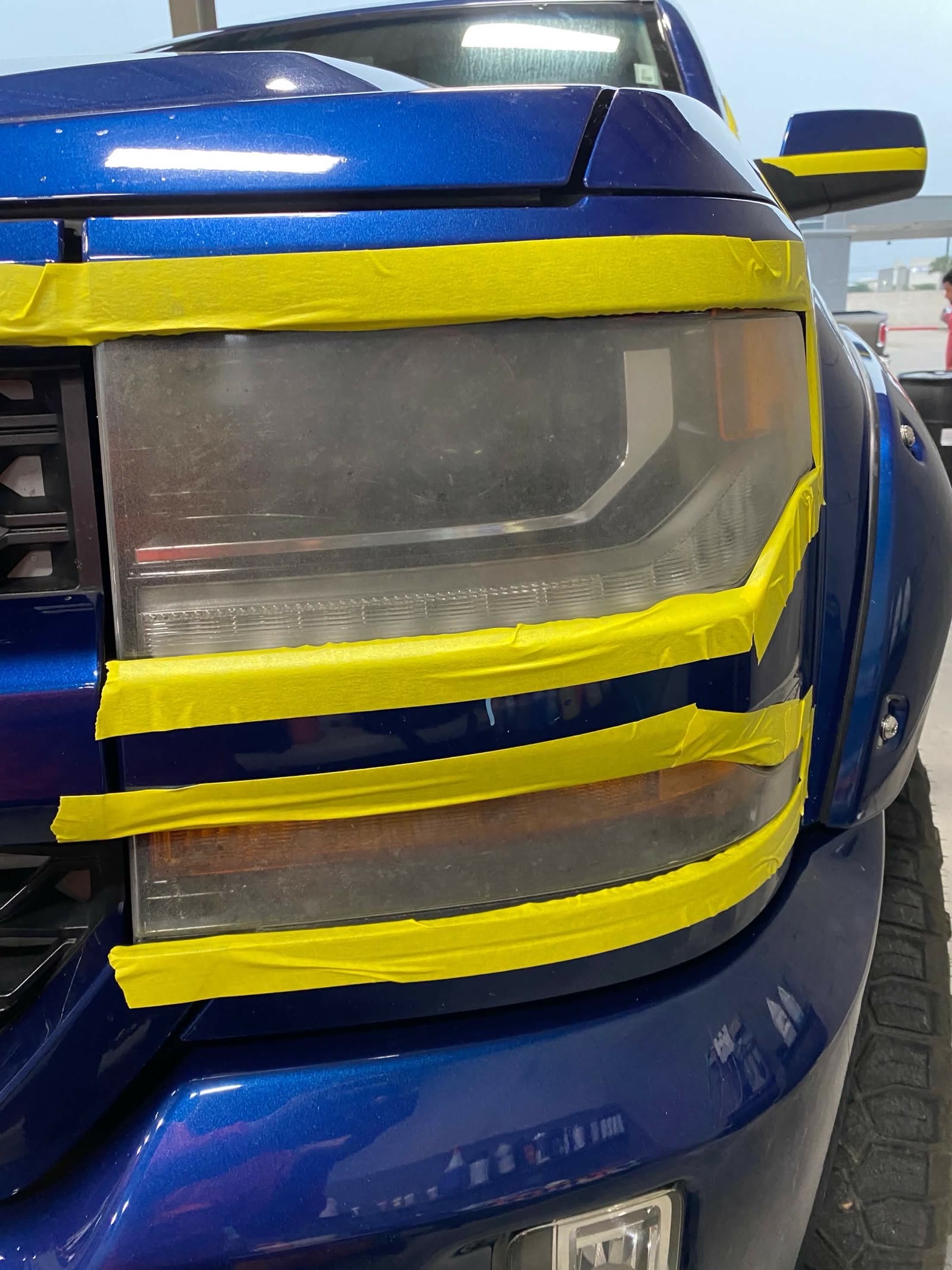 Blue pickup headlight masked with painter tape during restoration